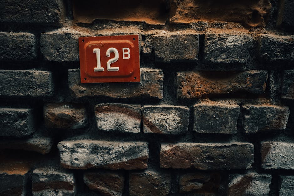 Vintage red door plate with 12B on a weathered brick wall