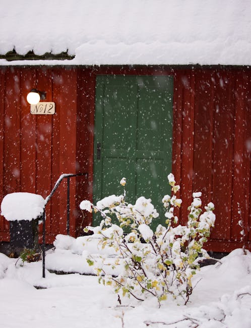 A snowy scene outside a red house with house number 12 visible
